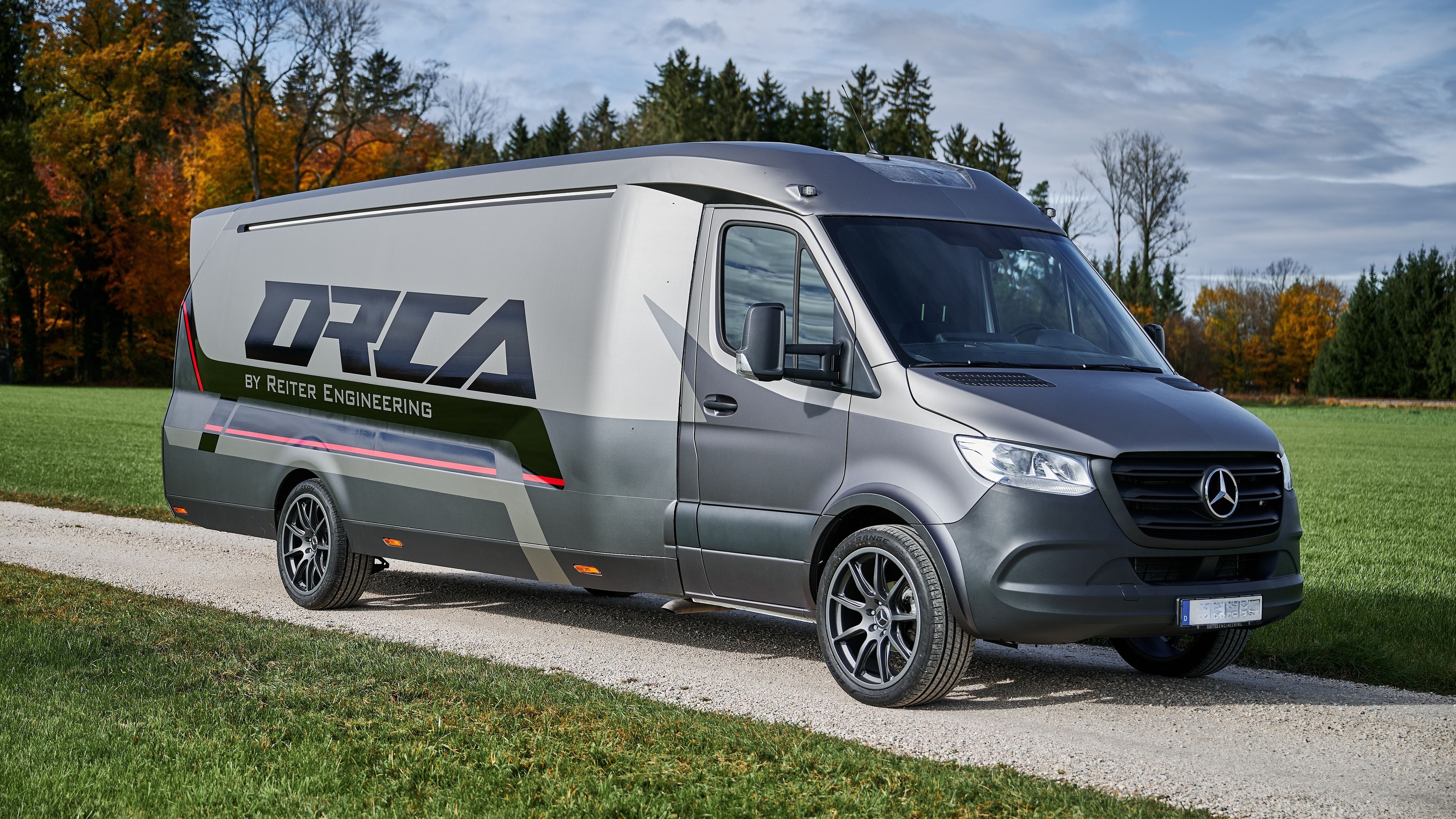 Schräge Frontansicht des ORCA Transporters auf Basis eines Mercedes-Benz Sprinter mit sportlichem Reiter Engineering Design und Alufelgen auf einem Feldweg.