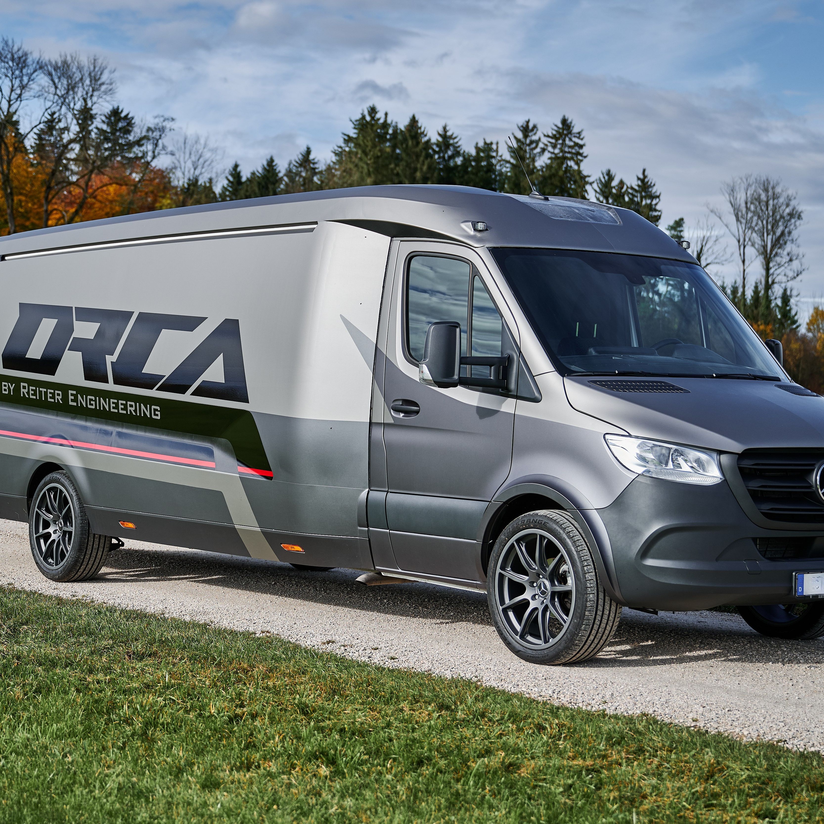 Schräge Frontansicht des ORCA Transporters auf Basis eines Mercedes-Benz Sprinter mit sportlichem Reiter Engineering Design und Alufelgen auf einem Feldweg.