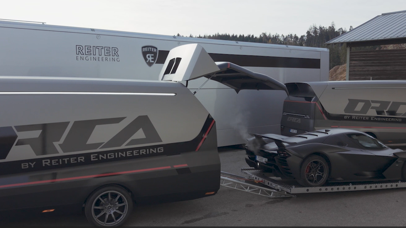 Ein mattschwarzer KTM X-BOW Sportwagen wird über eine Rampe in den futuristischen Orca Transporter von Reiter Engineering geladen.