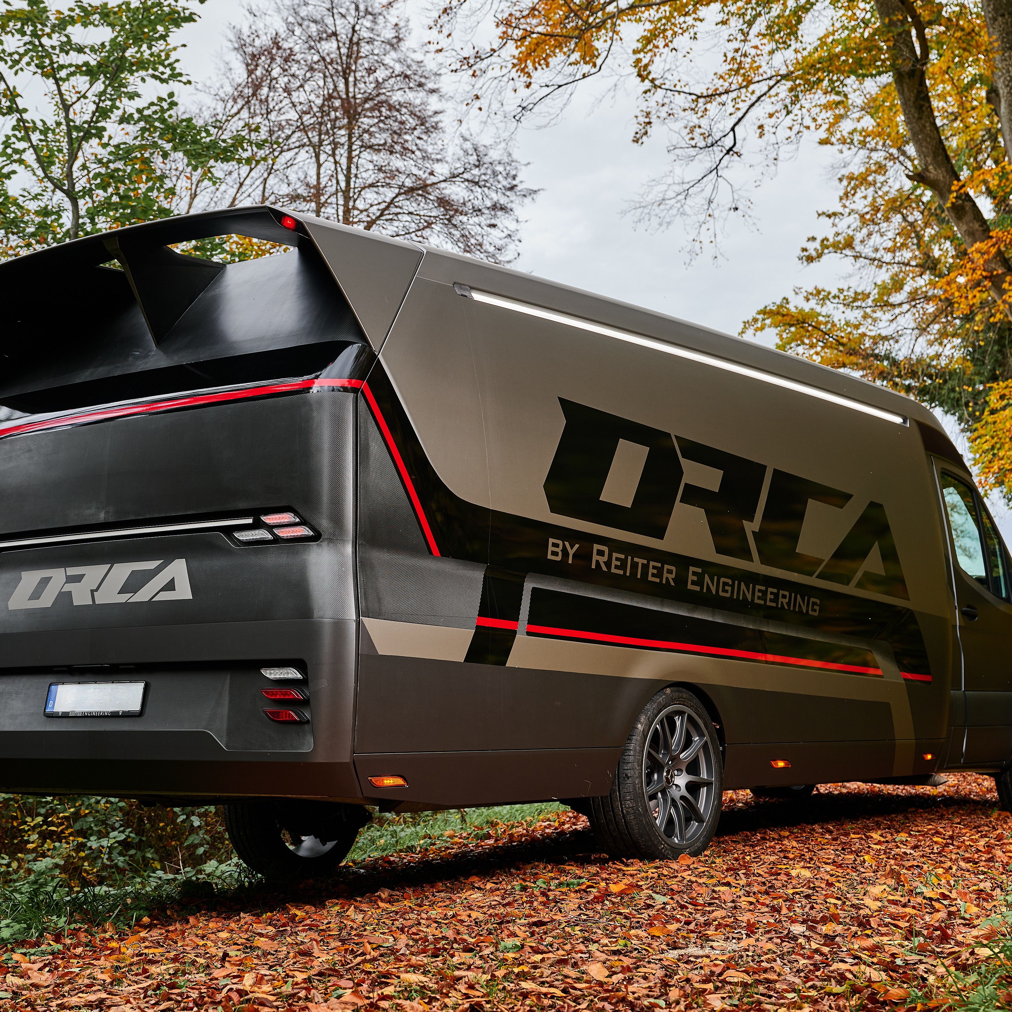 Rückansicht des ORCA Transporters von Reiter Engineering mit markantem Heckspoiler und Carbon-Elementen auf einem herbstlichen Waldweg