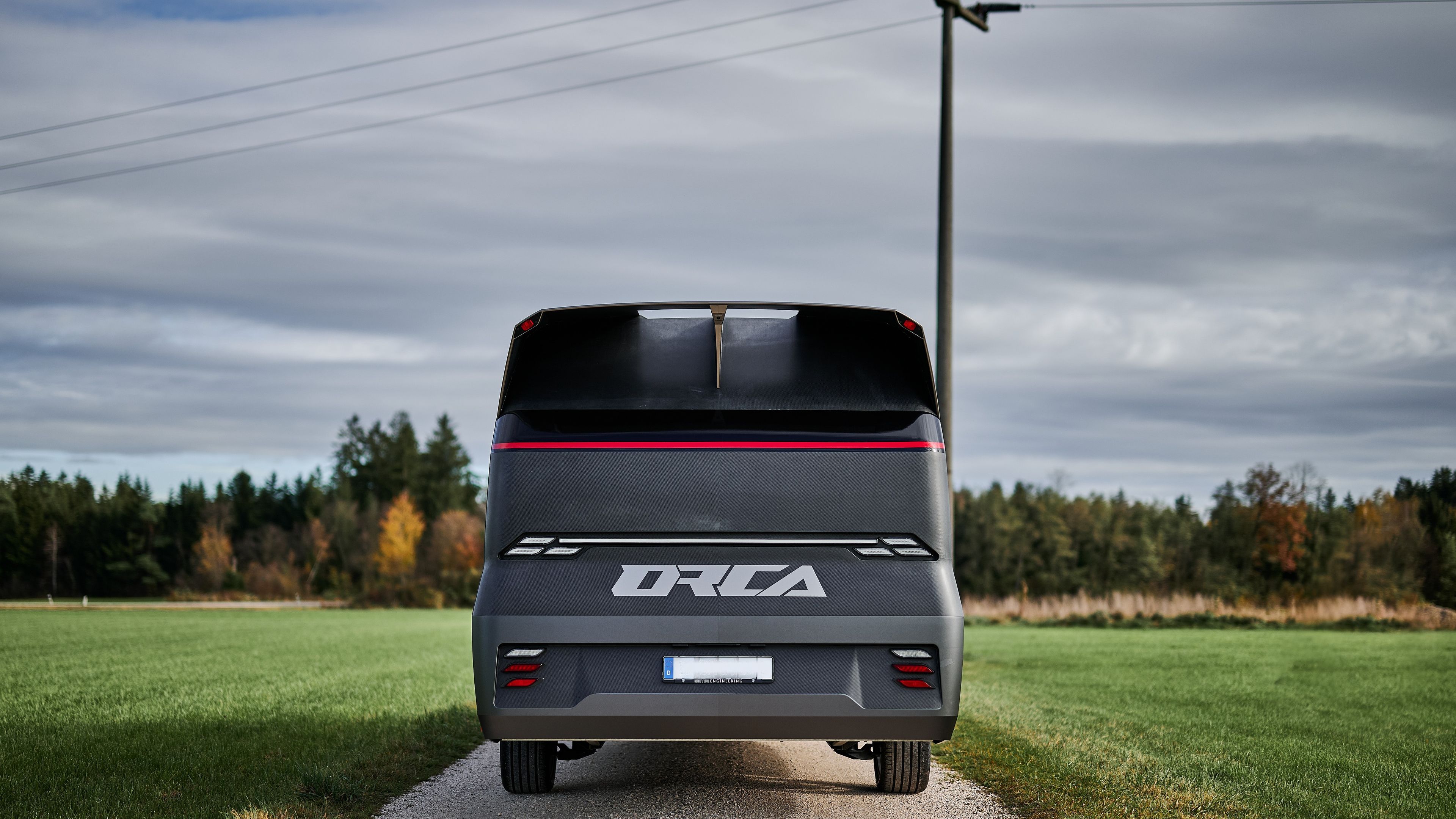 Geschlossene Heckansicht der Carbon-Heckstruktur des ORCA Leichtbau-Transporters mit Logo und Rücklichtern auf Feldweg