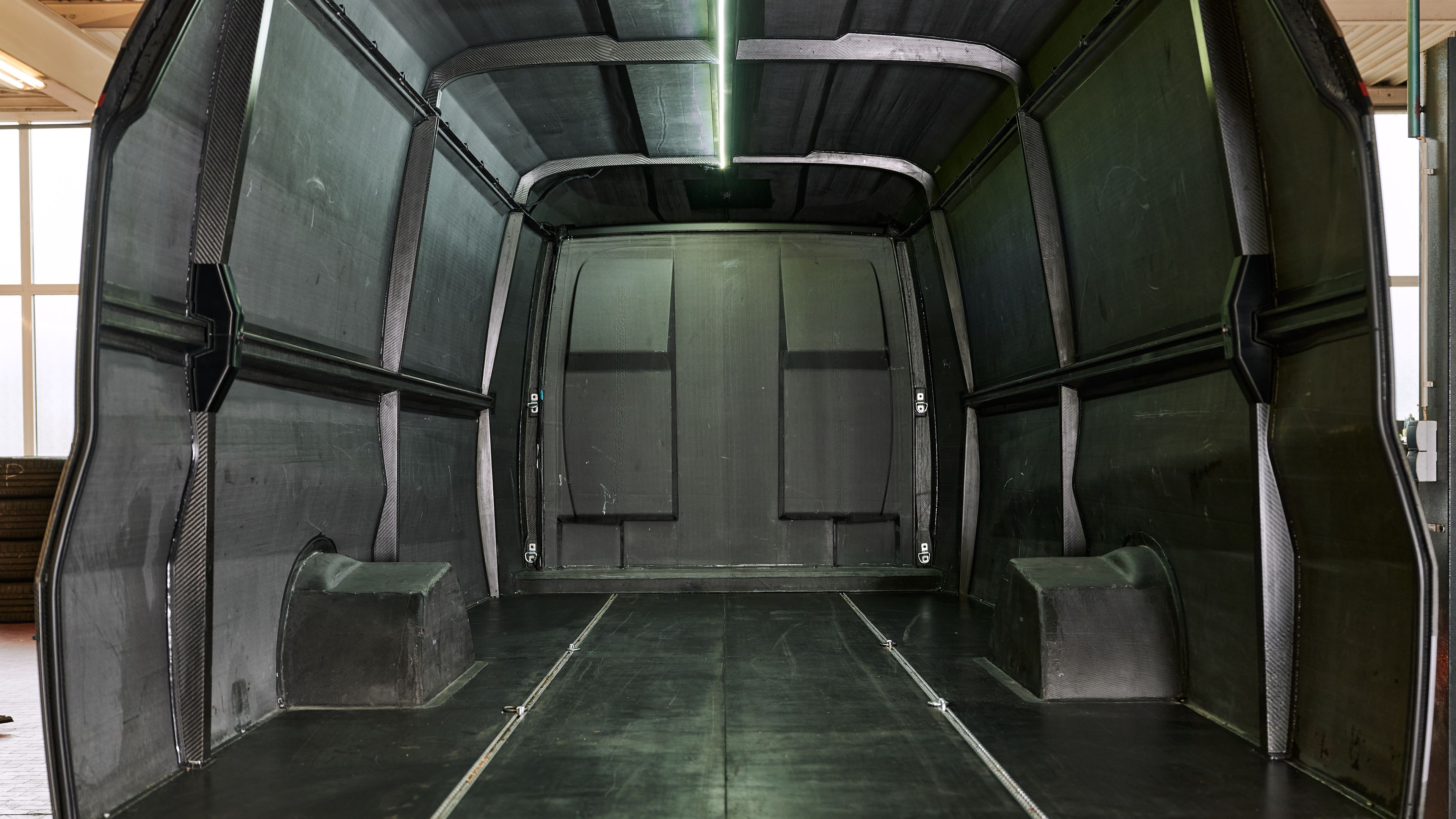 Innenansicht eines leeren Orca Transporters aus dunklem Carbon-Verbundwerkstoff mit integrierter Deckenbeleuchtung und Radkästen.