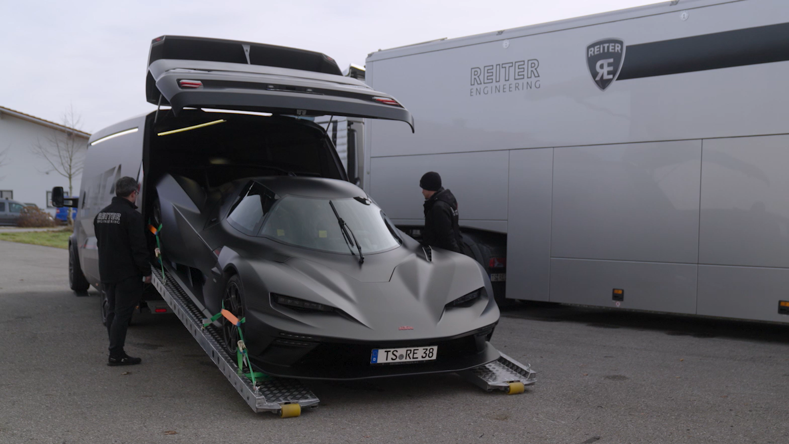 Ein schwarzer Rennwagen wird über Rampen in das Heck eines ORCA Transporters der Reiter Engineering Rennteam-Abteilung verladen